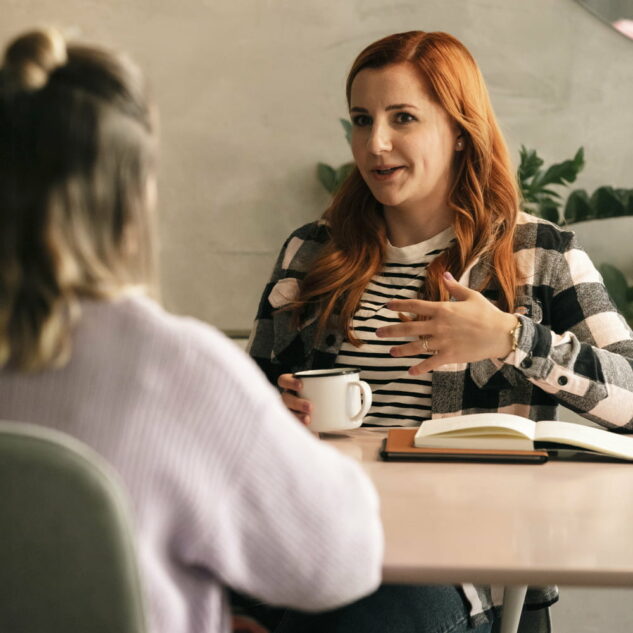 Two women having a conversation at a table in a coffee shop.