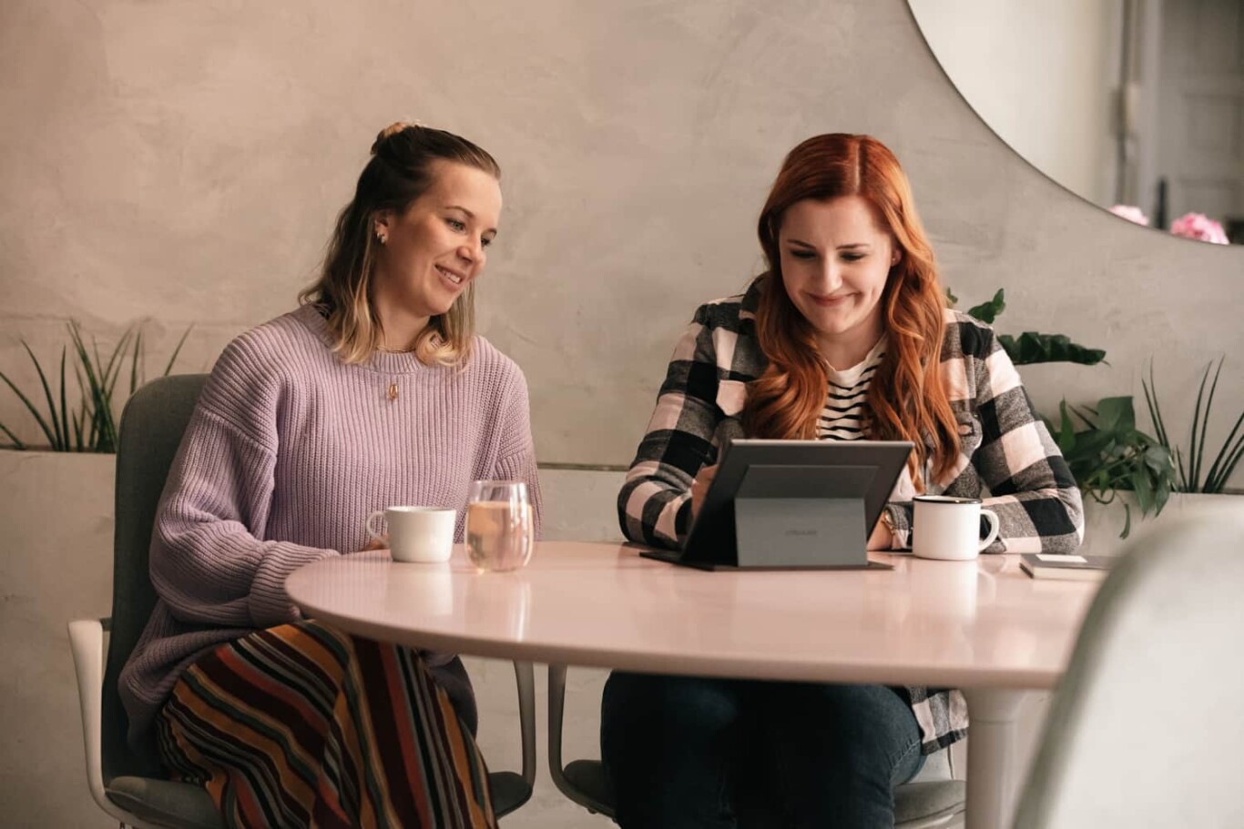 Two women having a conversation at a white table in a cafe.