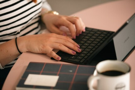 A person typing on a laptop at a pink desk with a coffee mug.