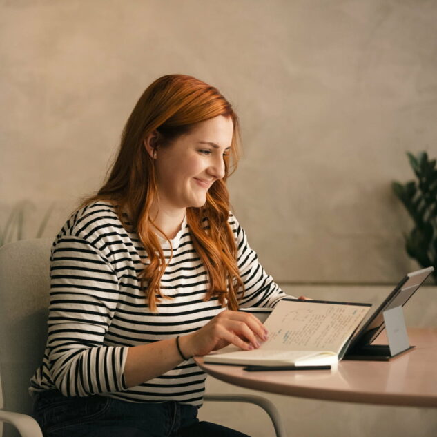 A person working on a laptop at a white desk with a plant in the background.