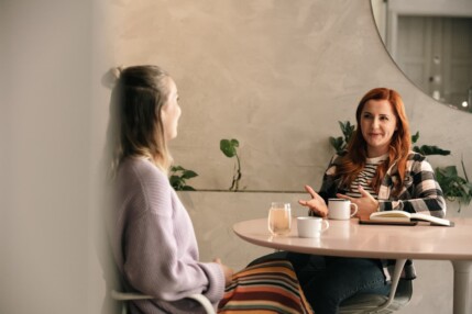 Two women having a conversation at a round table in a cafe.