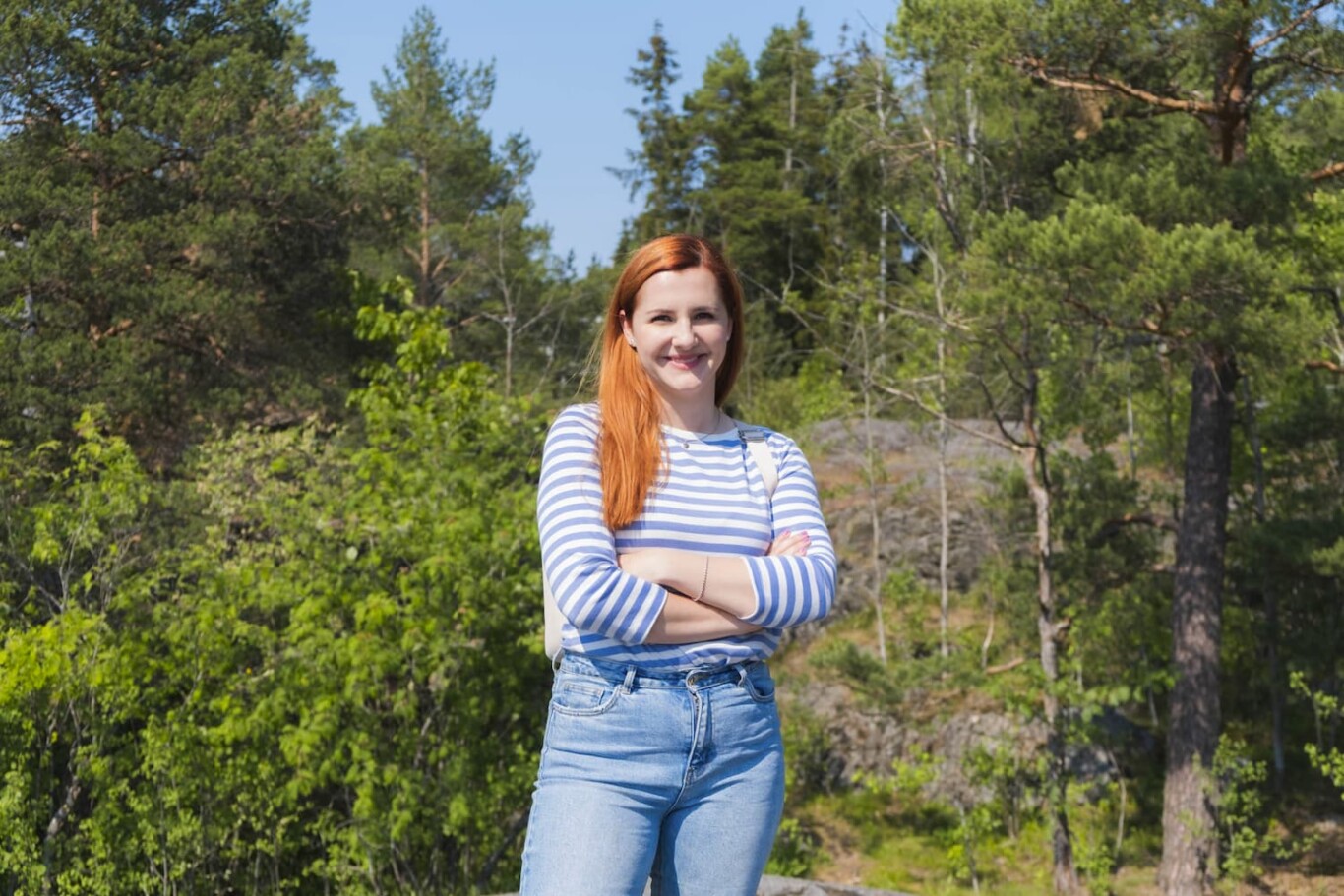 Karolina Numminen standing with her arms crossed in a sunny forest.