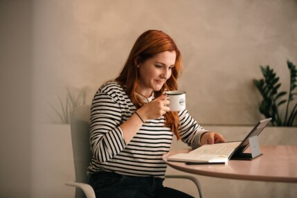 Karolina Numminen working on a laptop at a desk, holding a coffee mug.