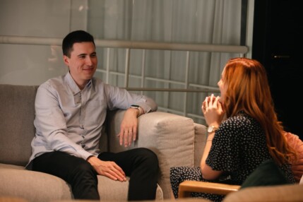 Two people having a casual conversation on a couch in a living room.