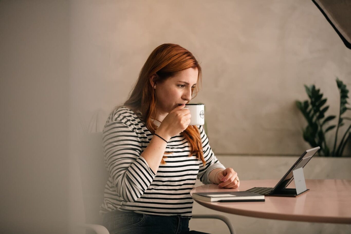 Karolina Numminen working on a laptop at a desk, holding a coffee mug.